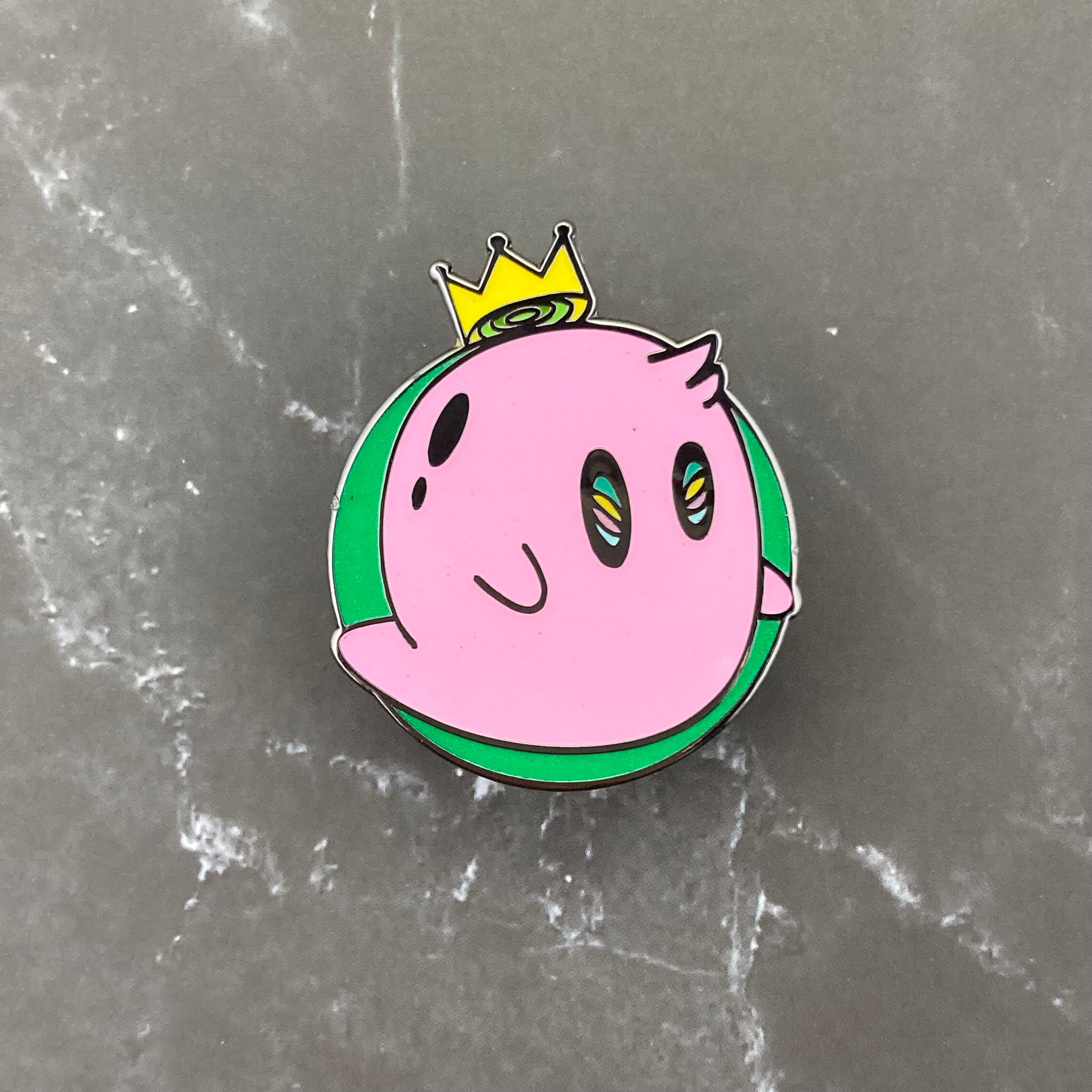 Pink ghost pin with yellowish crown in a green circle. Glows in the dark.